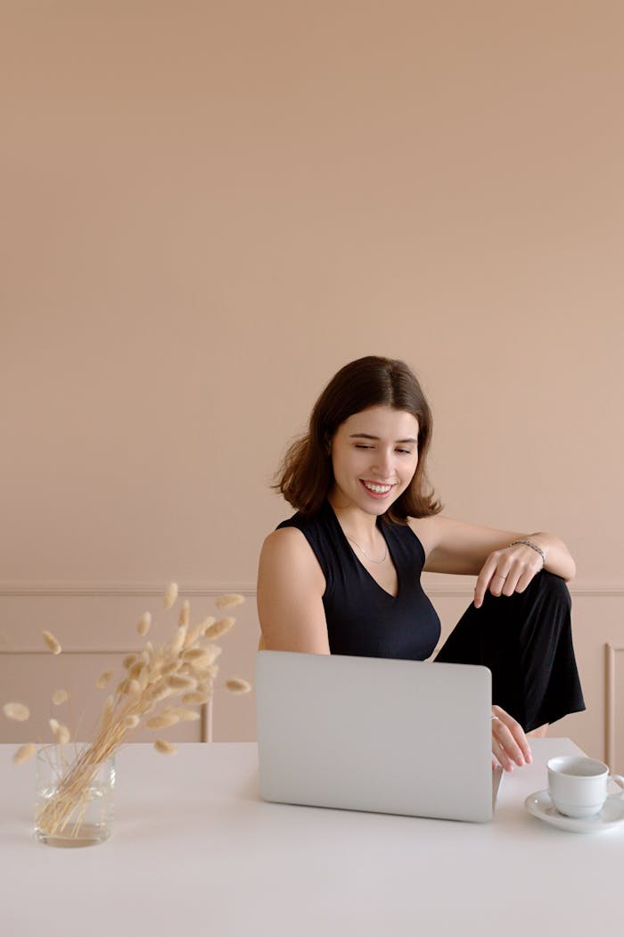 Woman in a Black Top Working on Her Laptop while Smiling